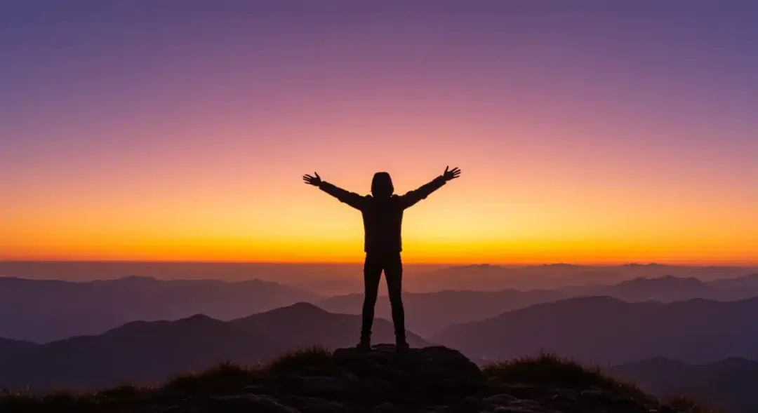 Person confidently standing on a mountain peak at sunrise