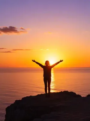 Woman embracing freedom overlooking sunset ocean vista, symbolizing letting go.