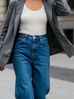 Woman wearing high-waisted wide-leg denim jeans with a white tank top and blazer in a city setting.