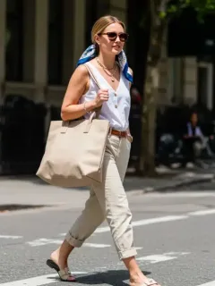 Stylish woman with spring 2026 fashion accessories: oversized tote, statement sunglasses, layered necklaces, silk scarf, and flat sandals.