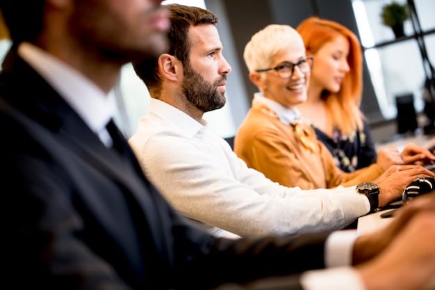 A group of employees sitting in a conference room, attentively listening to a cybersecurity training session. The presenter is visible on a screen with slides about phishing awareness and password security.