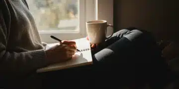 Serene person journaling gratitude with warm tea by a sunlit window.