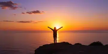 The Art of Letting Go: 5 Practical Steps to Release What No Longer Serves You This Month Woman embracing freedom overlooking sunset ocean vista, symbolizing letting go.