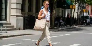 Stylish woman with spring 2026 fashion accessories: oversized tote, statement sunglasses, layered necklaces, silk scarf, and flat sandals.